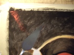 I'm using a palette knife to scrape red paint over the black background.
